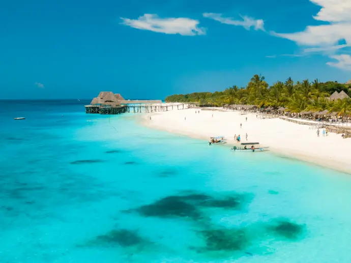 A white sand beach with palm trees and a wooden pier in Zanzibar, Tanzania